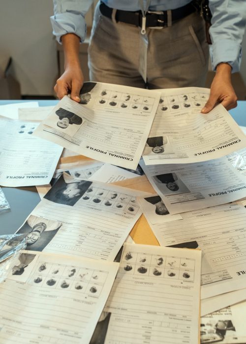 Hands of female investigator holding criminal profiles over desk with documents