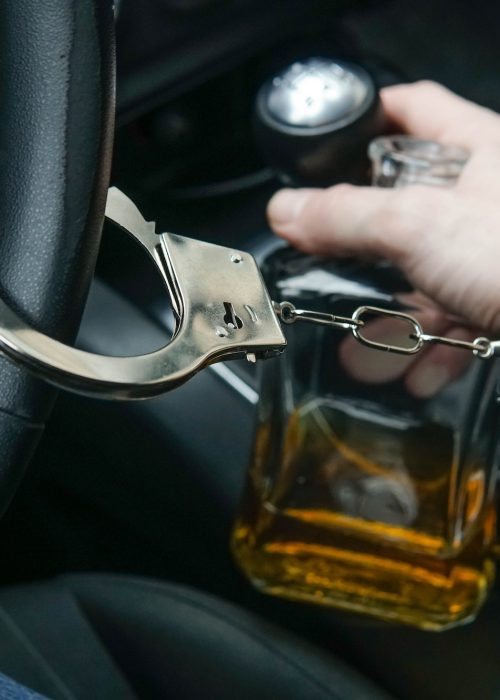 Man in handcuffs holds bottle of alcohol in car. Drunk driving concept. Don't drink and drive.